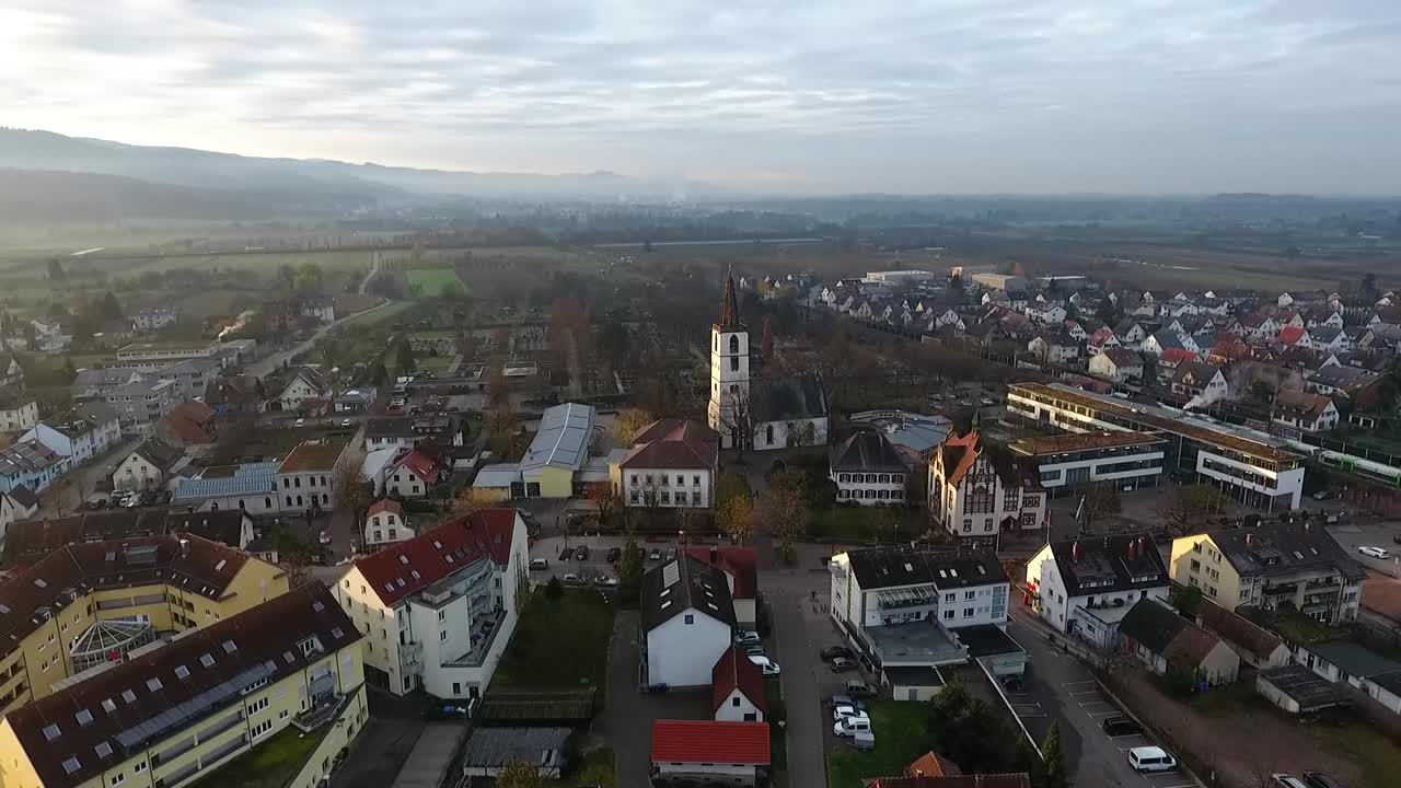 vista de la iglesia del pueblo de denzlingen, cementerio al fondo, sale un tren