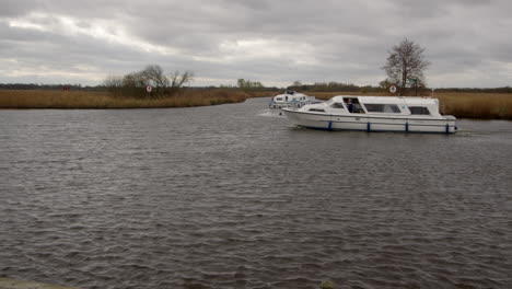 wide shot of a white norfolk broads cruiser boat passing the entry to south walsham broad