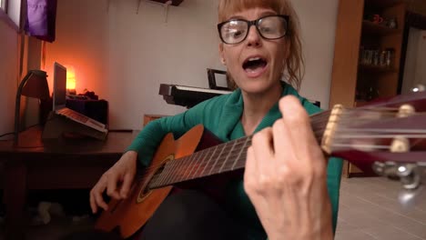 serenata de casa: mujer atractiva con gafas está tocando la guitarra y cantando