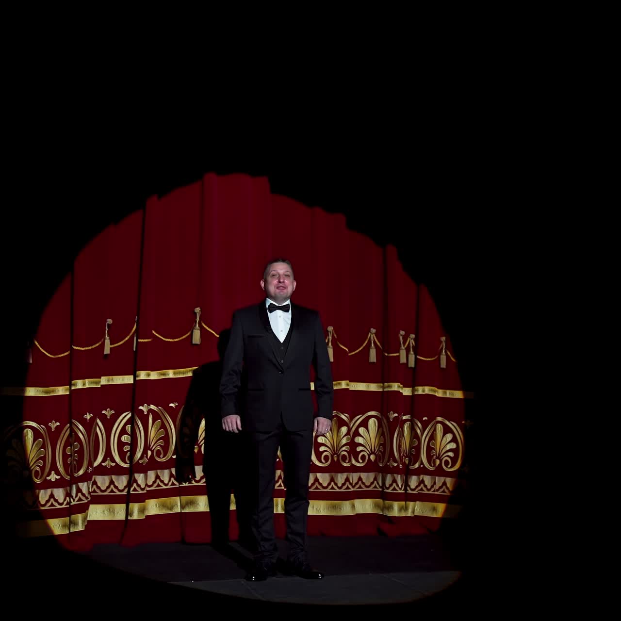 Actor appears on stage. Red curtains open and a theater host in suit comes on the scene on dark background in light spot
