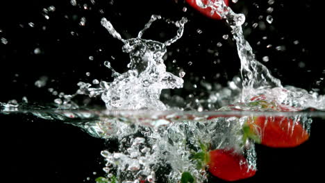 strawberries falling in water on black background