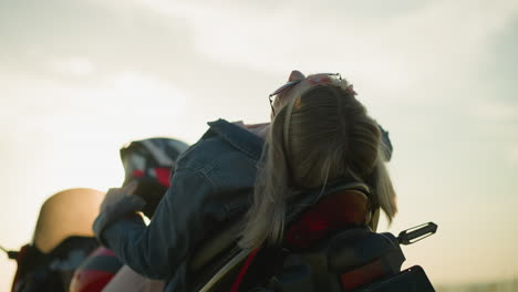 a woman wearing sunglasses rests on the seat of a bike with her face up to the sky, briefly touching her hair and then lowering her hand