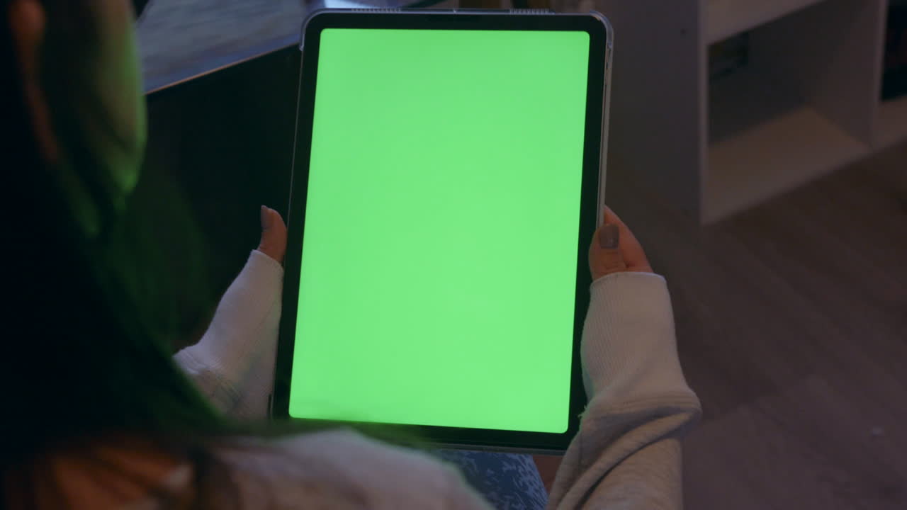 Kvinde holder iPad med grøn skærm i hænderne, set over skulderen.