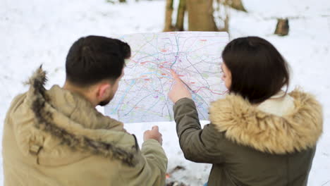 白人のカップルは雪の森で地図をチェックします。