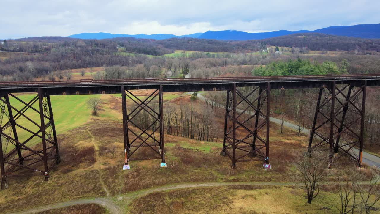 imágenes de video de drones aéreos de un viaducto de puente de tren que corre sobre un valle en las montañas appalachain a principios de la primavera en un día de nubes, rodeado de montañas y tierras de cultivo