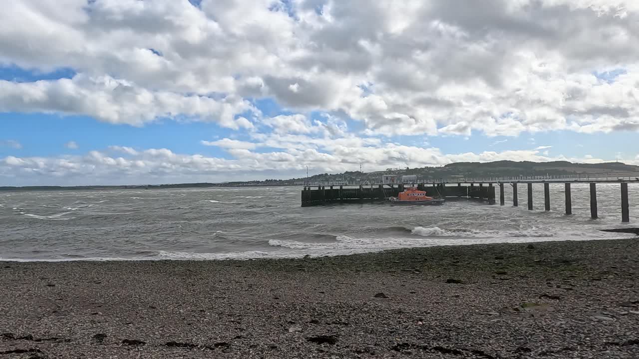 Small boat nears pier on windy, cloudy coastal shoreline