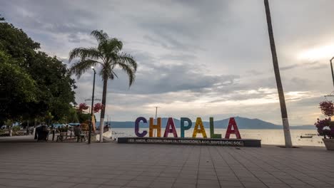 timelapse of the chapala sign with people passing by, set against palm trees and a bright sky in mexico, motion to the right as visitors take pictures