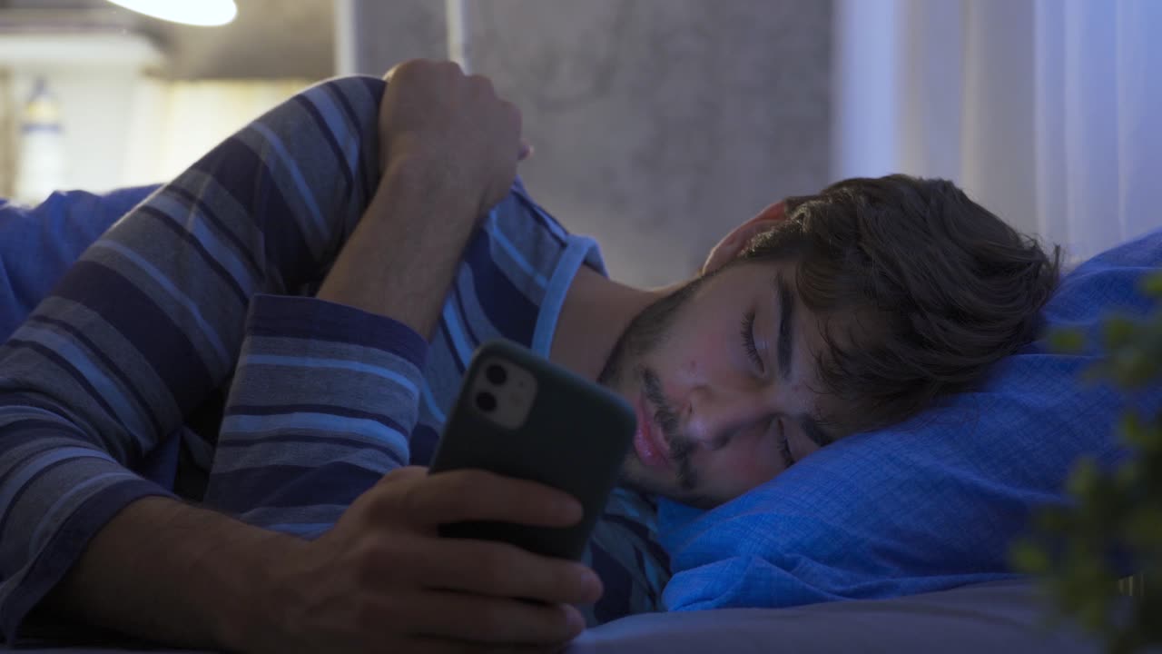 el hombre que mira el teléfono por la noche está durmiendo en su cama.