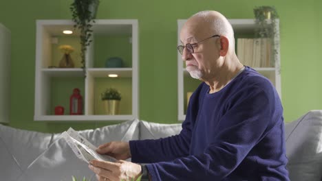 viejo intelectual sentado en el sofá en casa y leyendo noticias y artículos en el periódico.