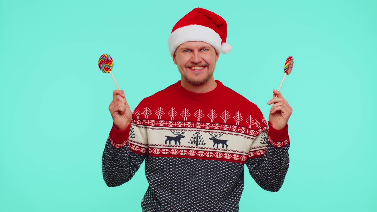 빨간 새해 스웨터를 입은 재미있는 남자는 사탕 줄무늬 막대사탕을 들고 그 뒤에 숨어서 장난을 치고 있습니다