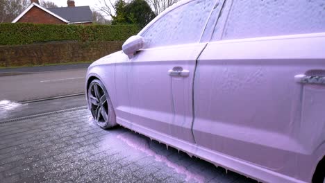 side view of a black car covered in pink snow foam