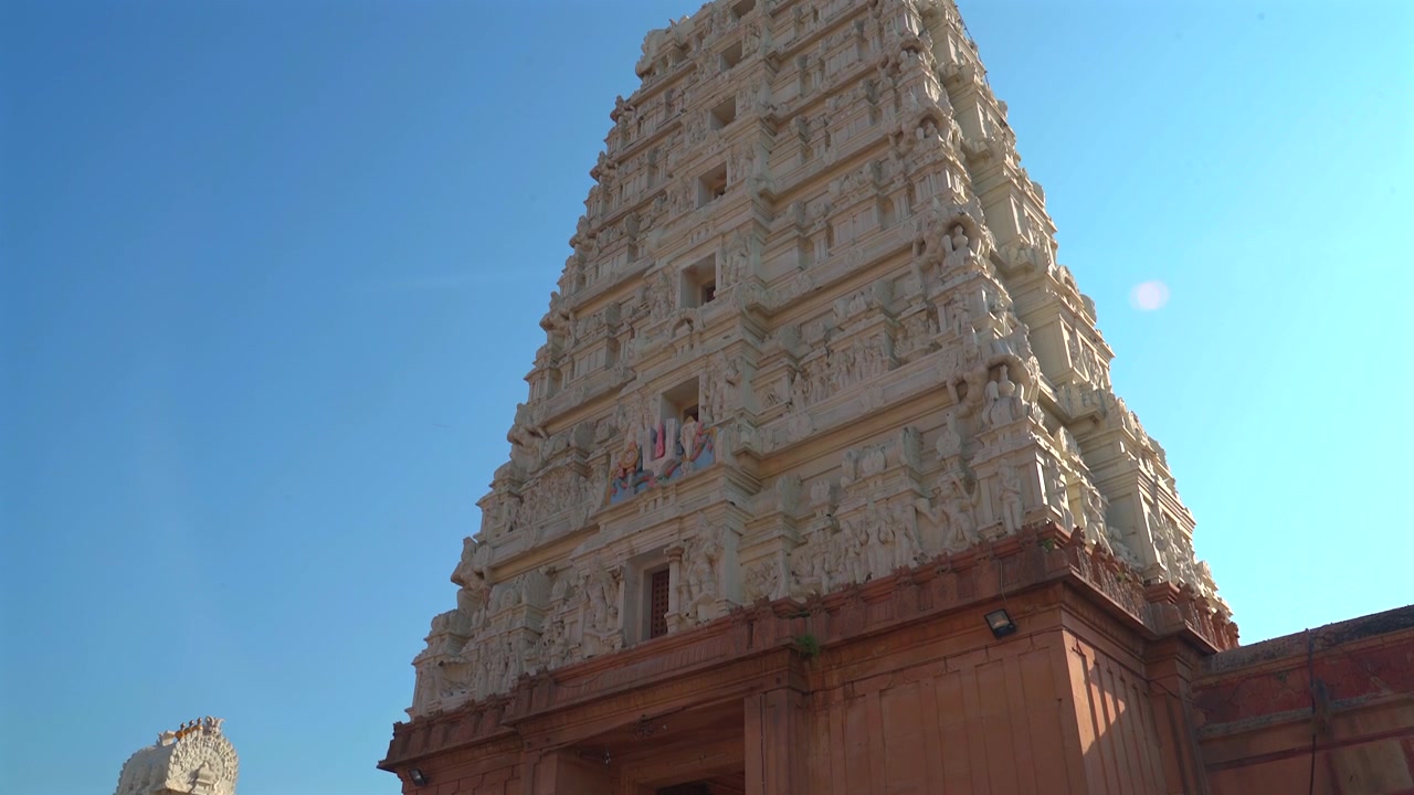 Pengambilan gambar sudut rendah menara gopuram batu putih berukir di Kuil Sri Ranganathji dengan latar langit biru cerah, di Vrindavan, India