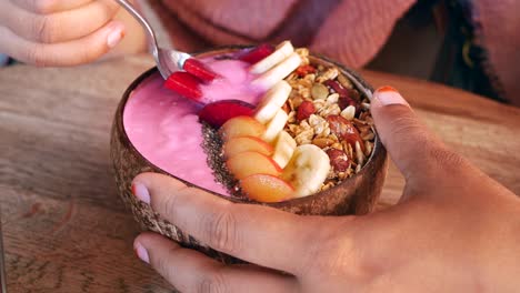 a person eating a healthy smoothie bowl with fruit and granola