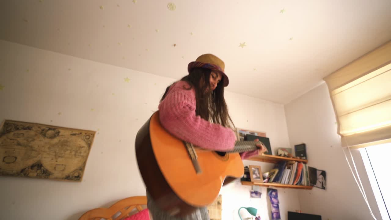 Giovane ragazza che salta sul letto con la chitarra nella camera da letto di casa.