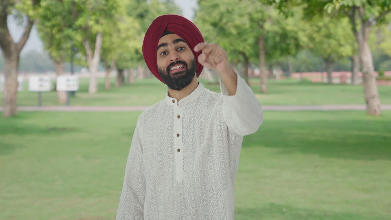 Uomo indiano Sikh felice che indica e chiama qualcuno al parco