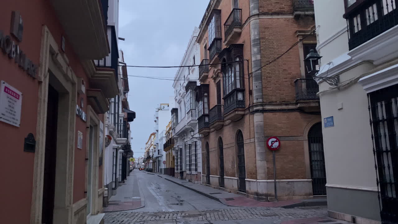 Rue vide dans le centre historique de Sanlucar de Barrameda, Espagne, montrant des bâtiments traditionnels et un pavé mouillé.