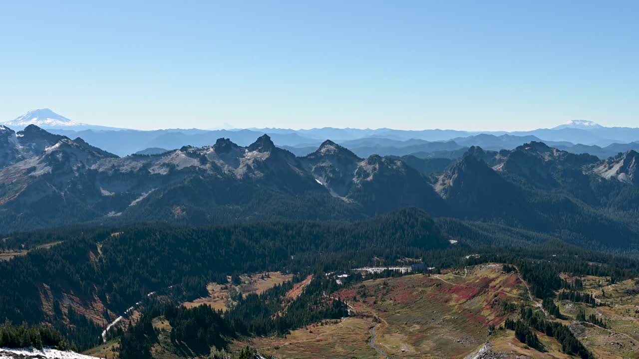 Aerial panorama of snow-dusted mountain ridges with distant view of Mount Rainier under a clear blue sky