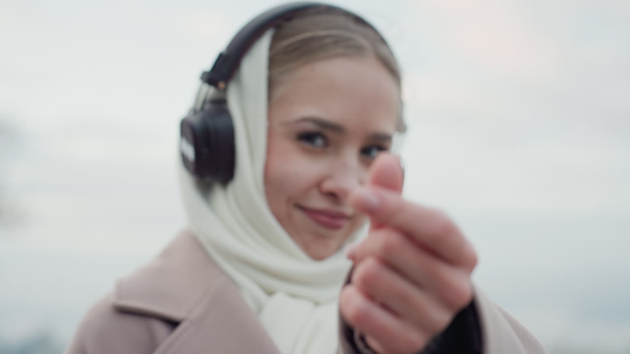 Donna che fa il gesto del cuore. Donna con le cuffie che sorride calorosamente. Primo piano di donna con un gesto allegro e accessori. Donna giocosa in abbigliamento invernale con cuffie e un sorriso dolce.