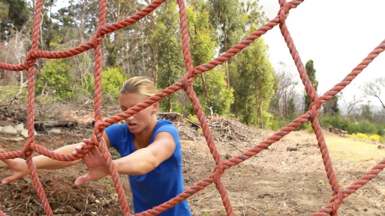 mujer en forma subiendo a una red durante una carrera de obstáculos