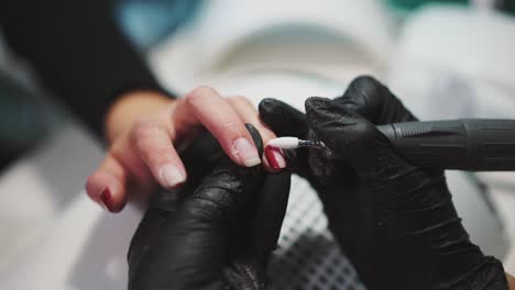 manicurist is removing red gel polish from the client's fingers with the using of professional equipment. beauty salon