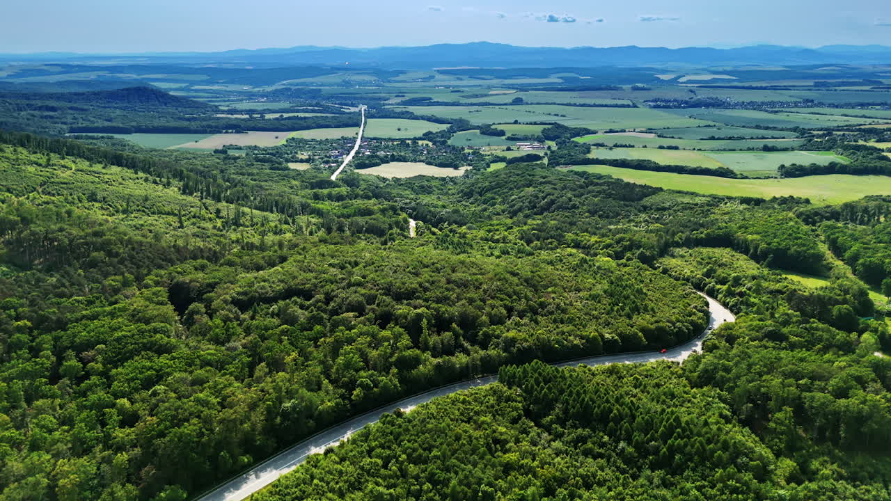 Hilly roads in lush scenery. Aerial view showcases green hills and winding roads under a clear sky in a serene rural area