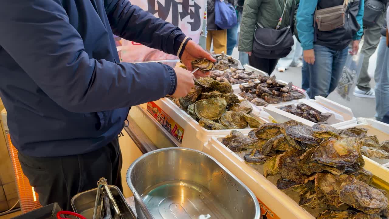 A vendor skillfully shucks fresh oysters at a busy outdoor seafood market in Tokyo