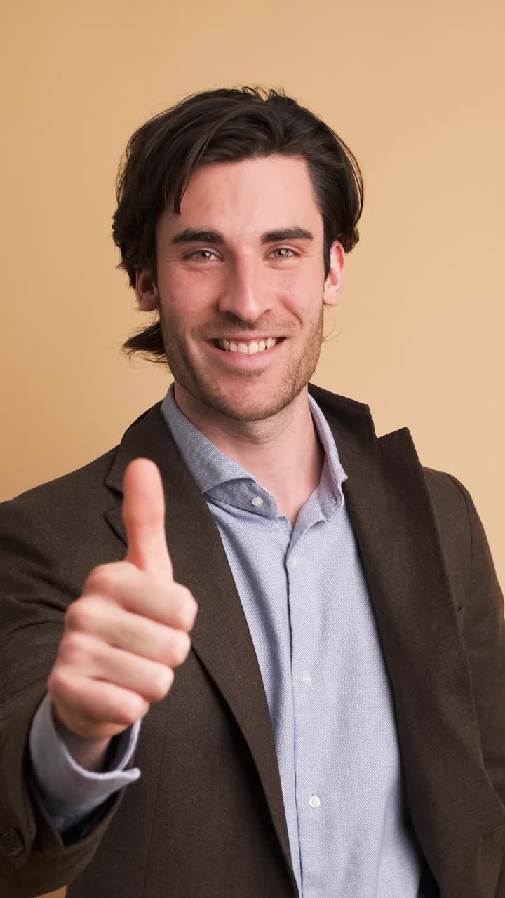 Happy businessman showing thumbs up in brown studio
