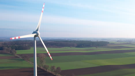 Luftaufnahme-Einer-Windkraftanlage-Mit-Rotierendem-Rotorblatt-Vor-Landwirtschaftlichen-Feldern-Bei-Sonnenuntergang-In-Europa