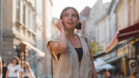 happy young woman in wireless earphones choosing, listening music in smartphone dancing outdoors