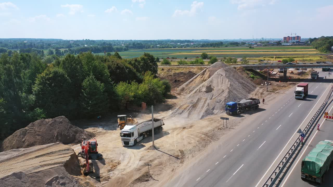 Heavy machinery with stones. New road with moving transport near the piles with stones. Trucks loading granite stones. Aerial shot.