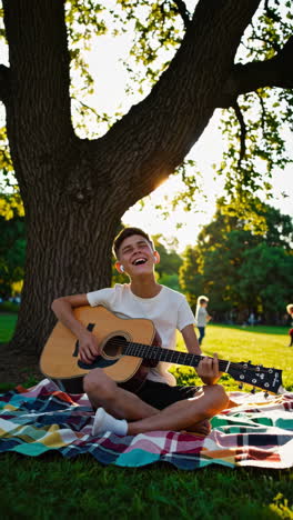 young man playing acoustic guitar outdoors in a park