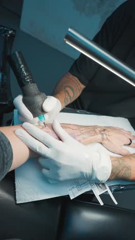 vertical - man in white gloves with machine tattooing half sleeve over stencil