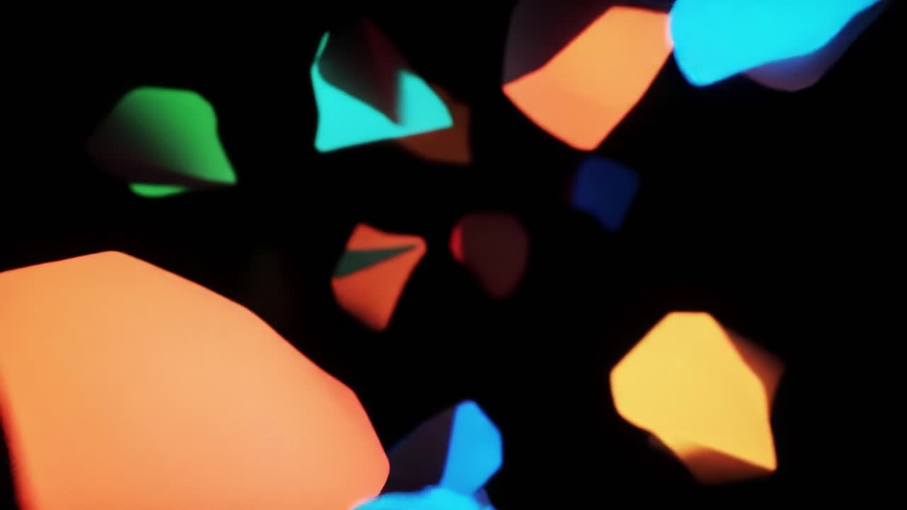 Brightly colored abstract shapes drift in a dark environment, creating a captivating ambience that draws the viewer in and provides a sense of wonder and exploration within the artistic display.