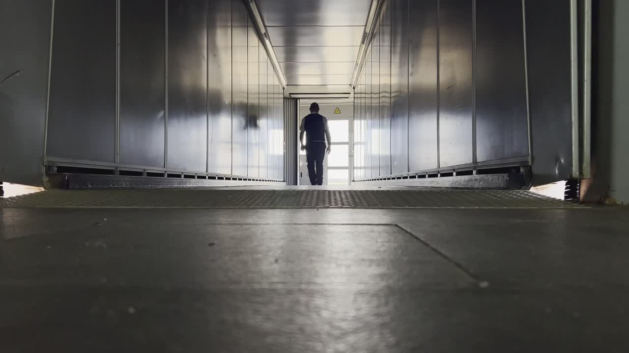 Rear view from a low angle of a male airport staff member walking away down an empty, metallic jet bridge. Departure and transportation industry concept