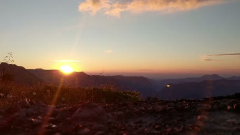 puesta de sol en la región alpina, el sol naranja se pone en el horizonte, la hierba y las flores soplan en el viento, la cámara está en un ángel bajo cerca del suelo, las nubes en el cielo