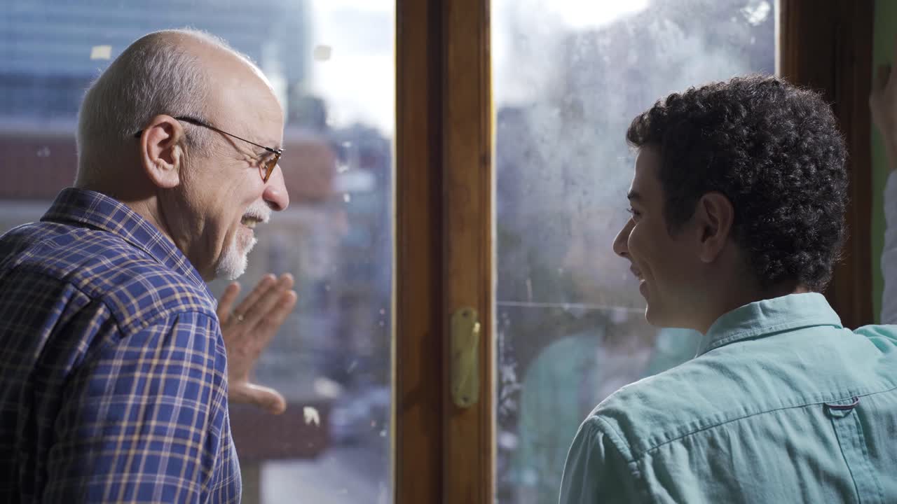 Elderly grandfather and grandson happily chatting in front of the window.