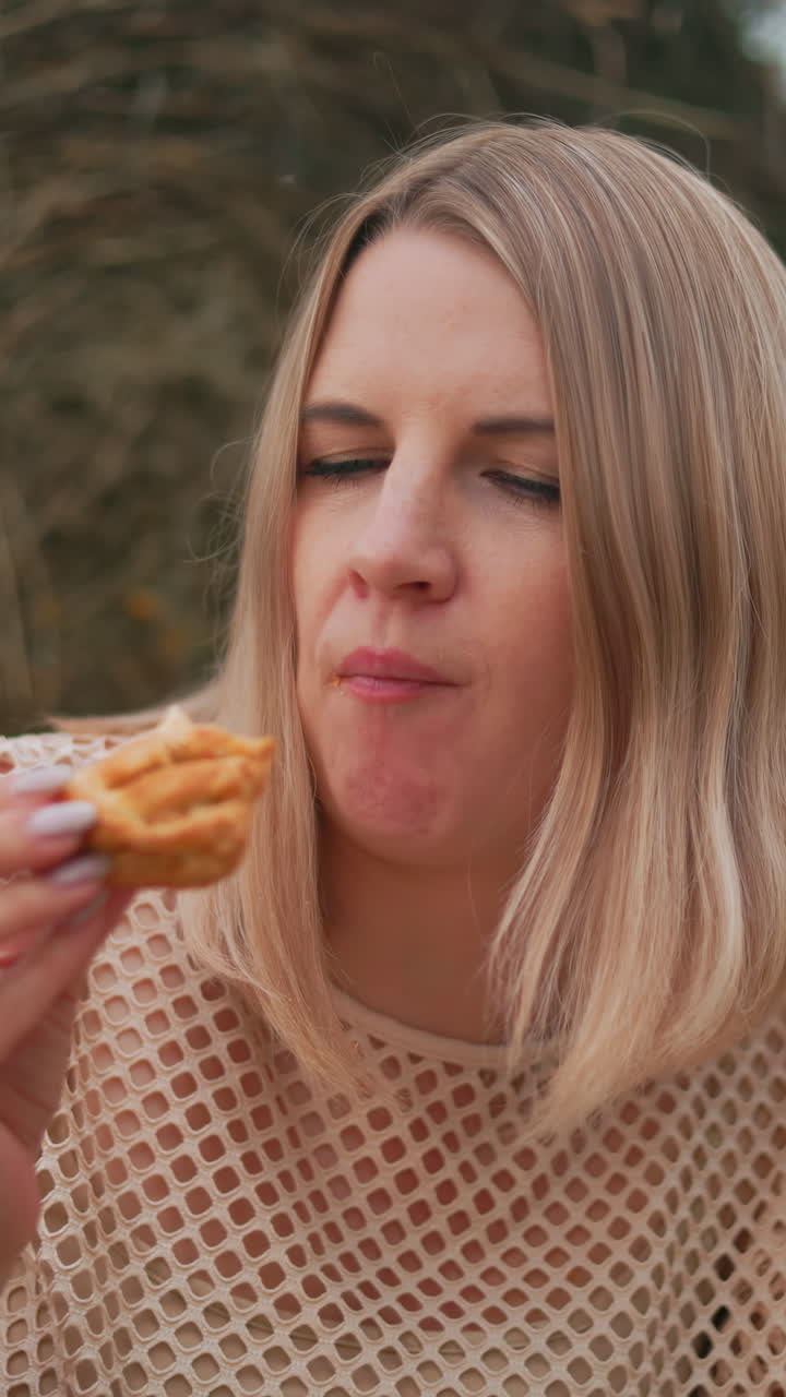 joven en camiseta net saboreando su pastel crujiente mientras está sentada en un campo abierto, el momento pacífico al aire libre captura una atmósfera serena con la naturaleza en el fondo