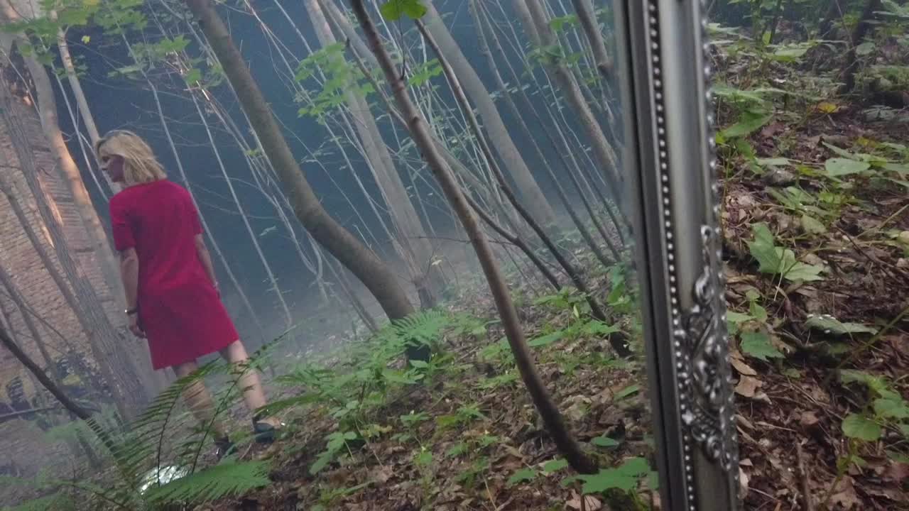 Fantastic slow motion cinematic shot of a young girl mirroring in a old mirror standing in a red dress lonely in a foggy forest. Foto video shoot on lost places in nature 1080, 24p by Philipp Marnitz