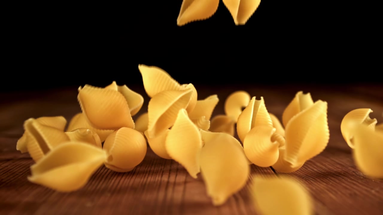 Trockene Conchiglie-Nudeln fallen auf einen rustikalen Holztisch