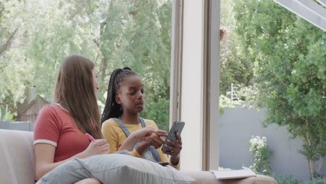 happy diverse teenage female friends sitting on couch and using smartphones in slow motion