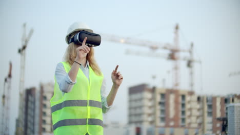 Porträt-Einer-Inspektorin,-Die-Die-Arbeit-Von-Bauarbeitern-Mithilfe-Einer-Virtual-Reality-Brille-Analysiert.-Eine-Frau-Mit-Helm-Und-Schutzweste-Steht-Mit-Einer-VR-Brille-Da-Und-Bewegt-Ihre-Hände