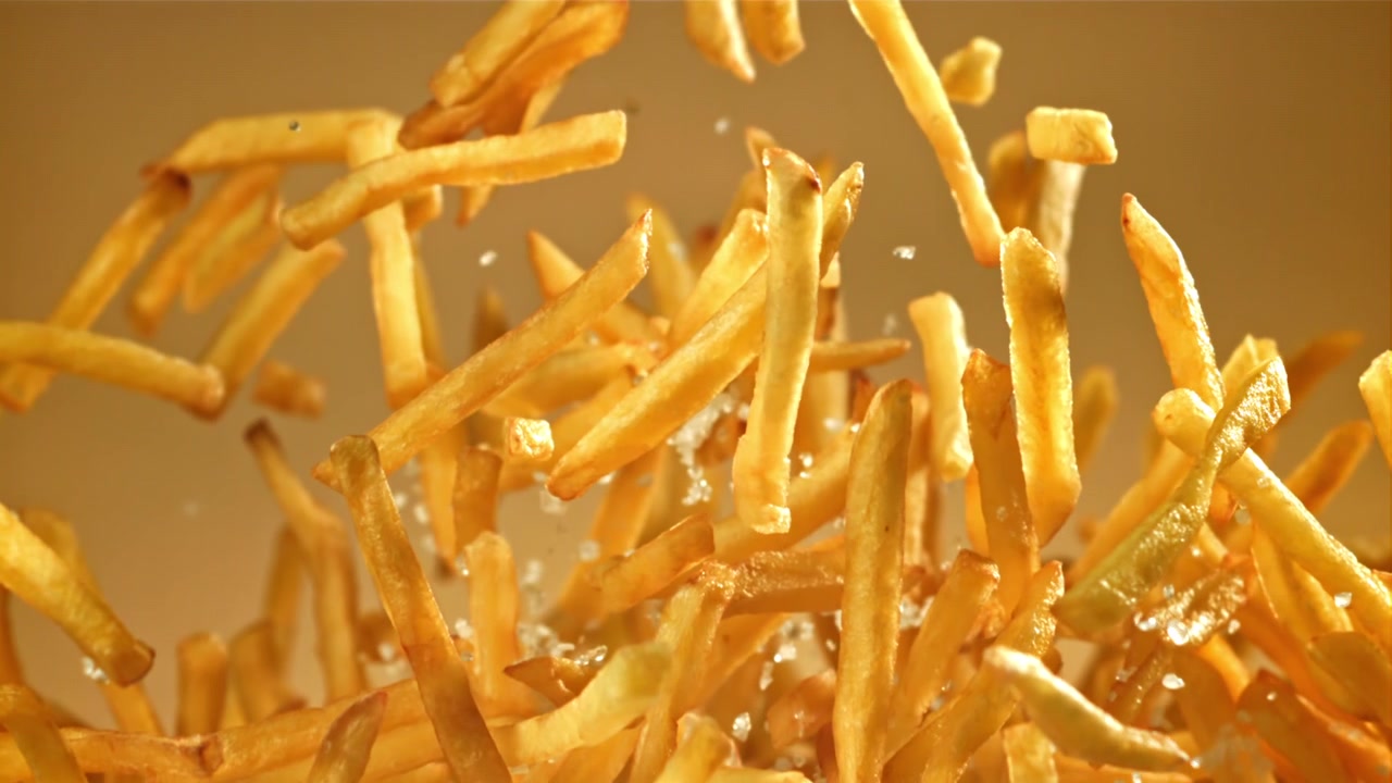 Goldene Pommes Frites und Salzkristalle fallen in Zeitlupe
