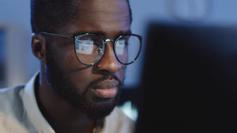 Close-Up-View-Bored-Young-Man-In-Glasses-Sitting-In-Front-Of-The-Computer-Screen-And-Looking-Sleepy-In-The-Office-At-Night