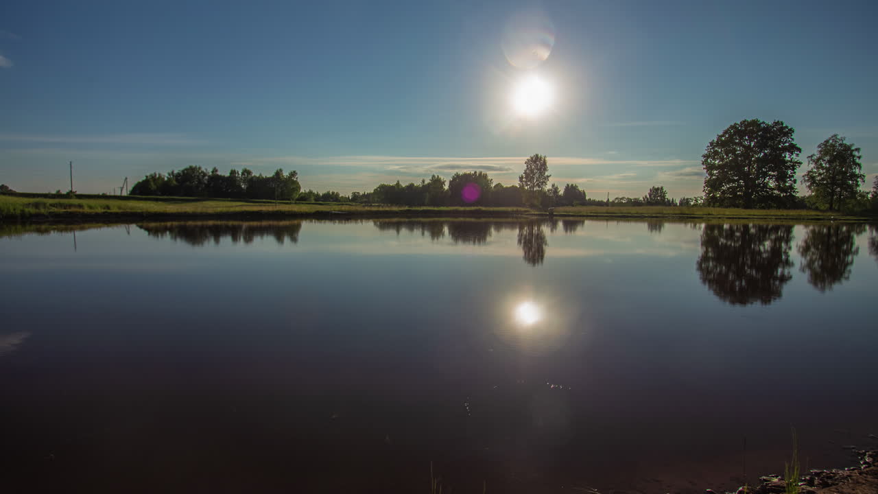 toma estática de la hermosa puesta de sol de verano en un lapso de tiempo sobre un lago rodeado de paisaje rural