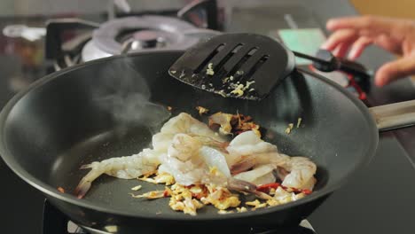 a girl is adding raw peeled shrimps to a hot pan with frying chili and garlic, homemade cooking in the kitchen