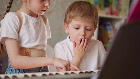el niño bostea aburrido de la lección de música de piano con su hermana