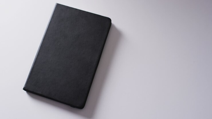 Detailní záběr na zavřenou černou knihu s místem pro text na bílém pozadí ve zpomaleném záběru.