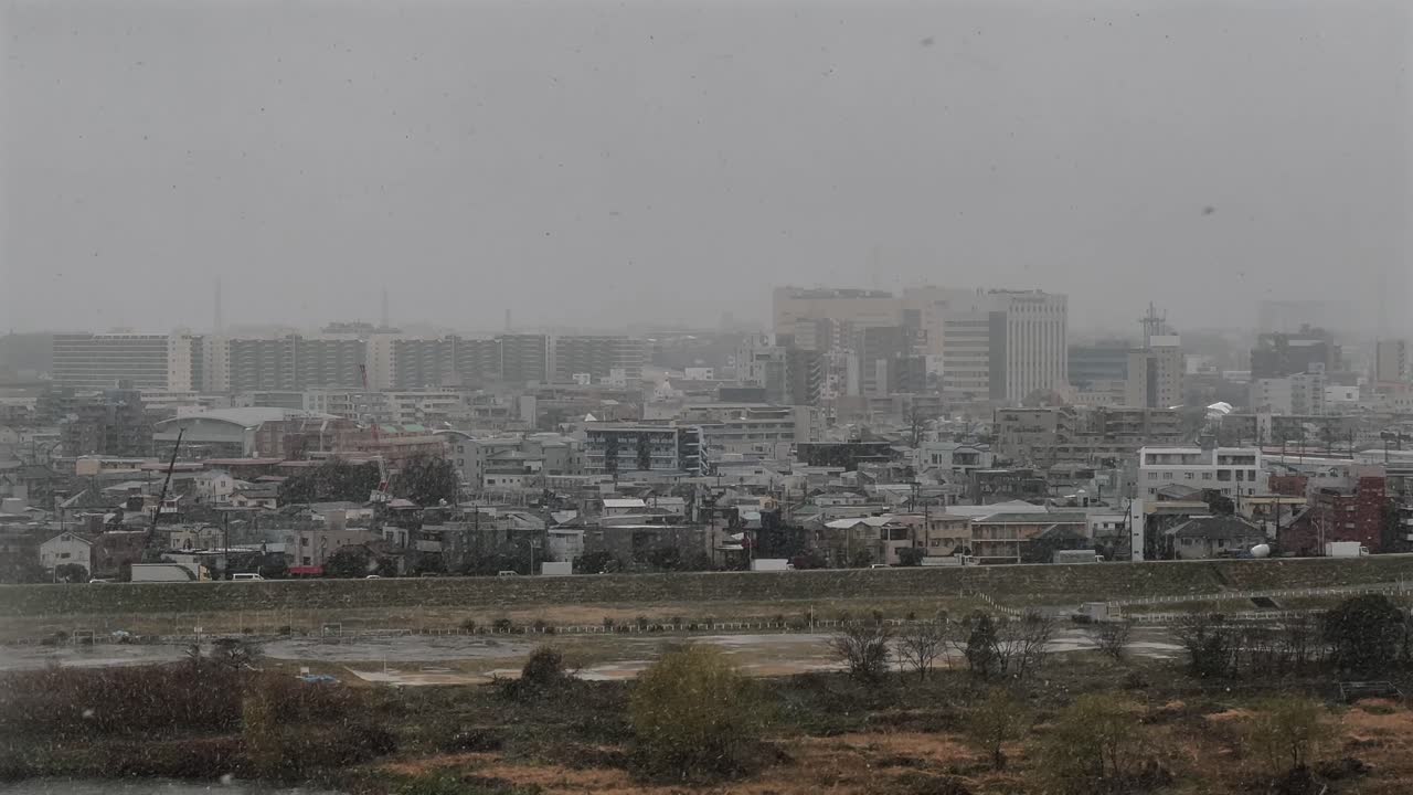High-rise view of Futakotamagawa on a snowy day, overlooking the Tamagawa River. Snowflakes drift through the grey, overcast sky, capturing a rare and serene winter scene in Tokyo