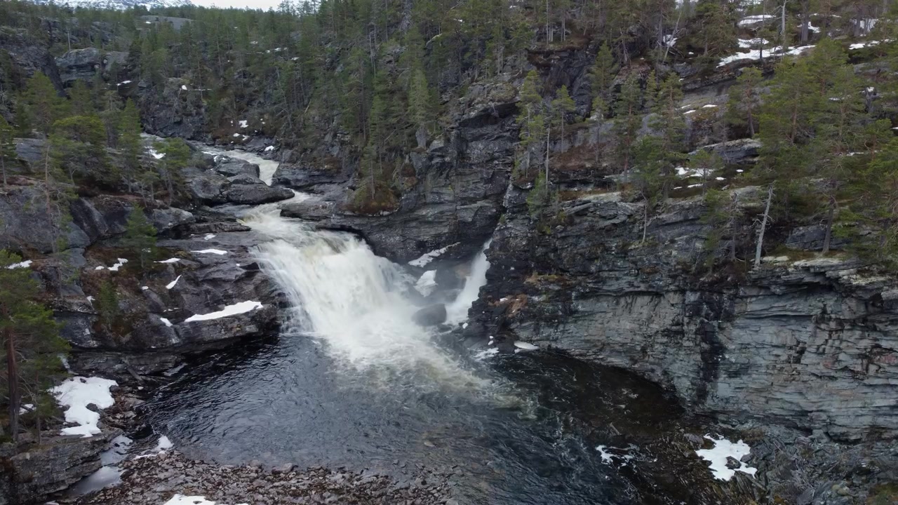 Foss som fosser ned i et elvebasseng omgitt av steinete klipper og bartrær i Norge