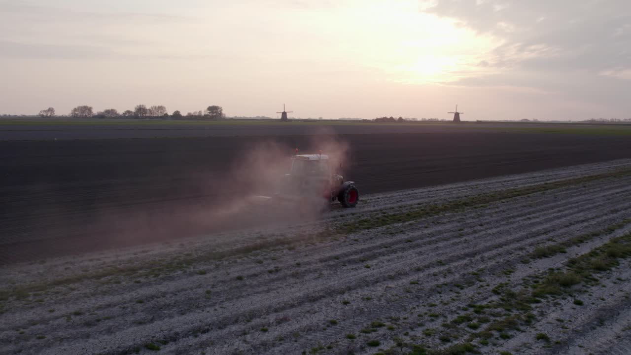 Vista aérea de trator à luz da manhã perto de moinho de vento e igreja, zona rural da Holanda